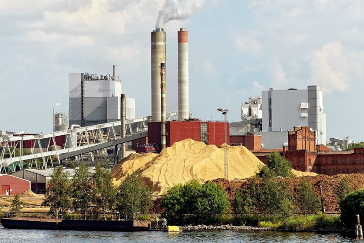 Riverfront paper mill with large wood chip storage pile