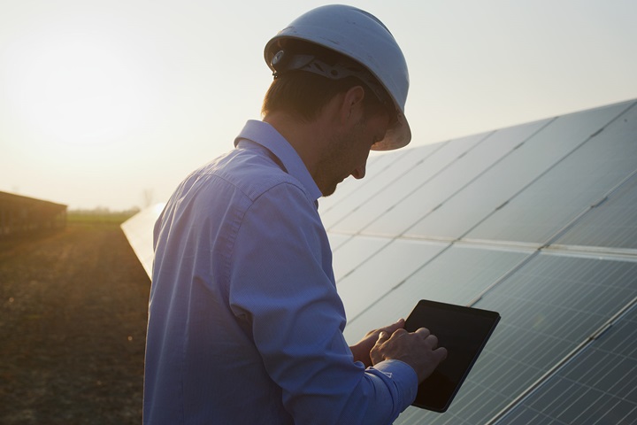 Worker with tablet standing in front of solar panels